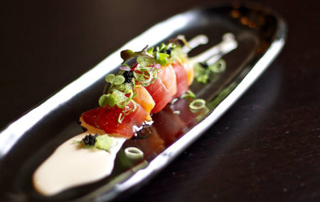 tuna sushi with scallions and white sauce on black plate