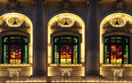 Three illuminated windows with stain glass red green and yellow a panels on ornate building