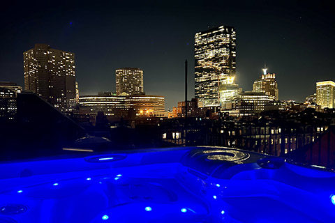 Roof top hot tub overlooking the dark blue sky and twinkling city at night