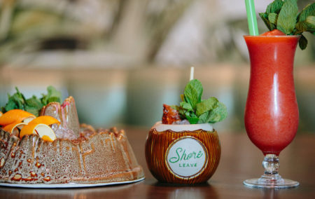 three cocktails one in a volcano dish one is a coconut with mint garnish and one tall red drink