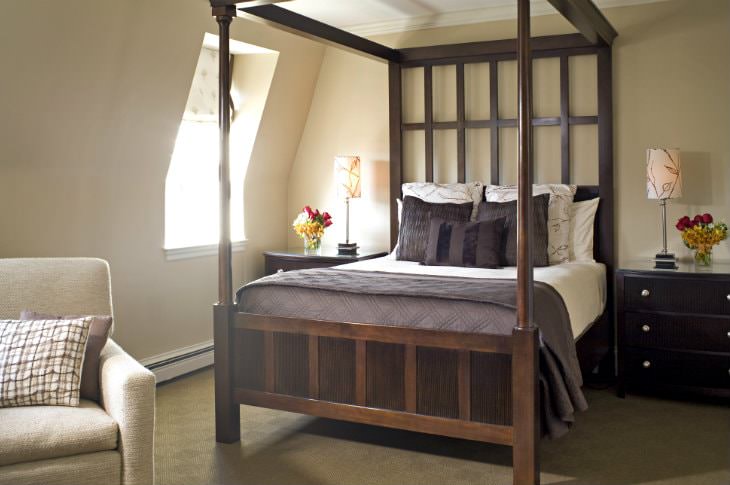 Elegant beige guest room with dark wood four-poster bed, and matching wood nightstands with lamps