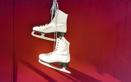 two white ice skates hanging by laces on a red background