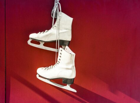 two white ice skates hanging by laces on a red background