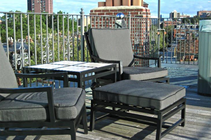 Roof top deck with black and gray chairs and ottoman and silver metal railing overlooking the city